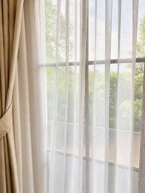 Una ventana con cortinas translúcidas y vistas al verdor exterior.