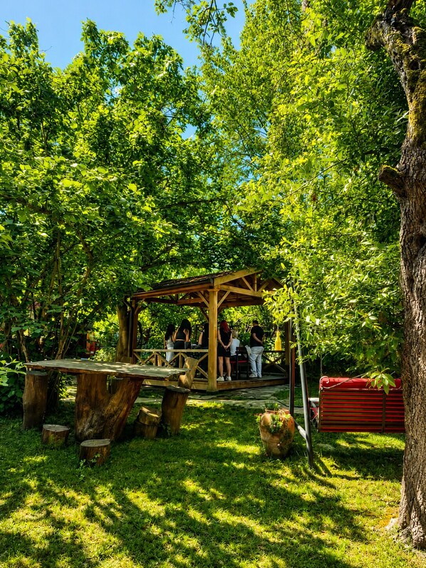A wooden gazebo in a lush green park with people around it.