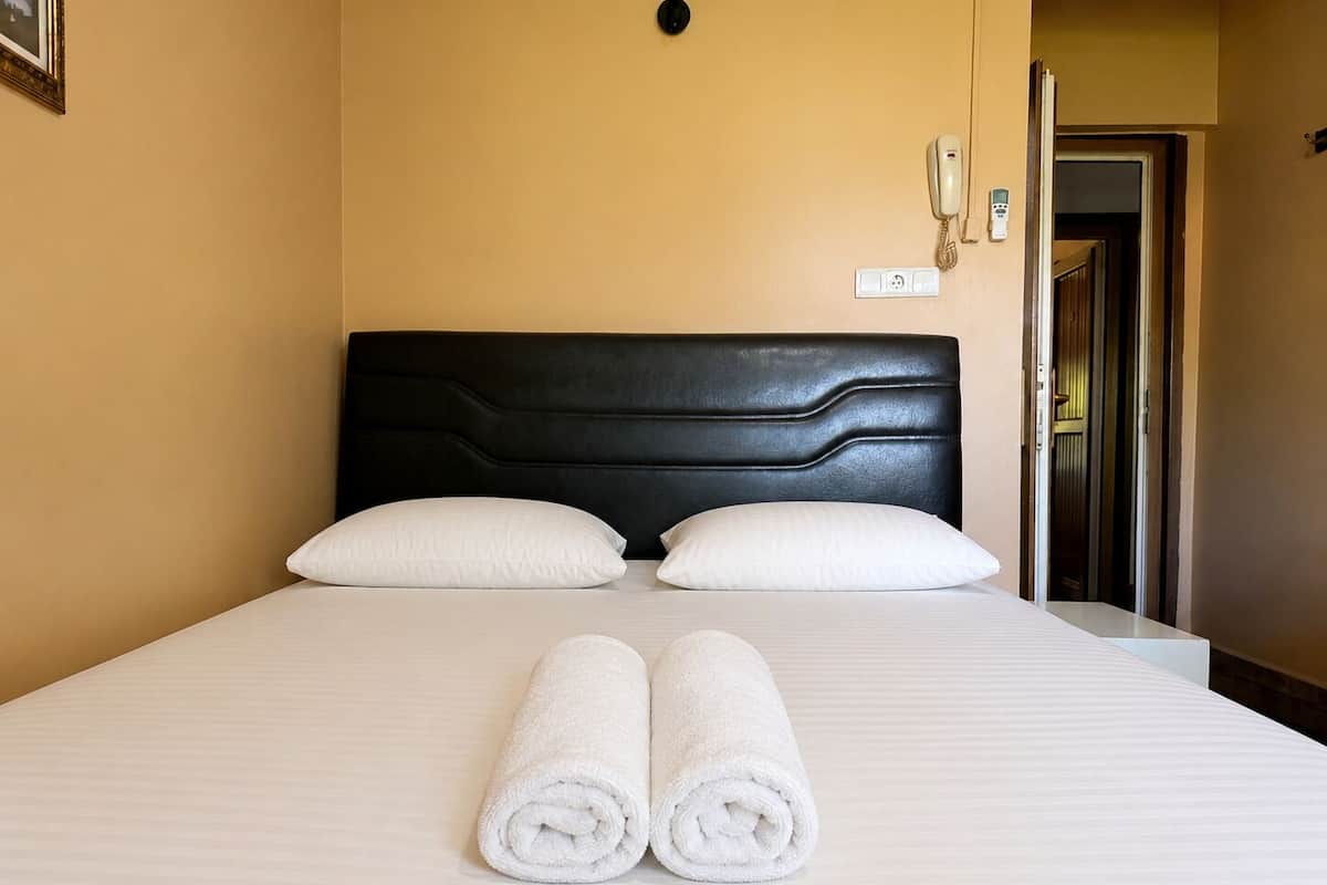 Una habitación de hotel con una cama, dos almohadas, un cabecero, un enchufe y una puerta.
