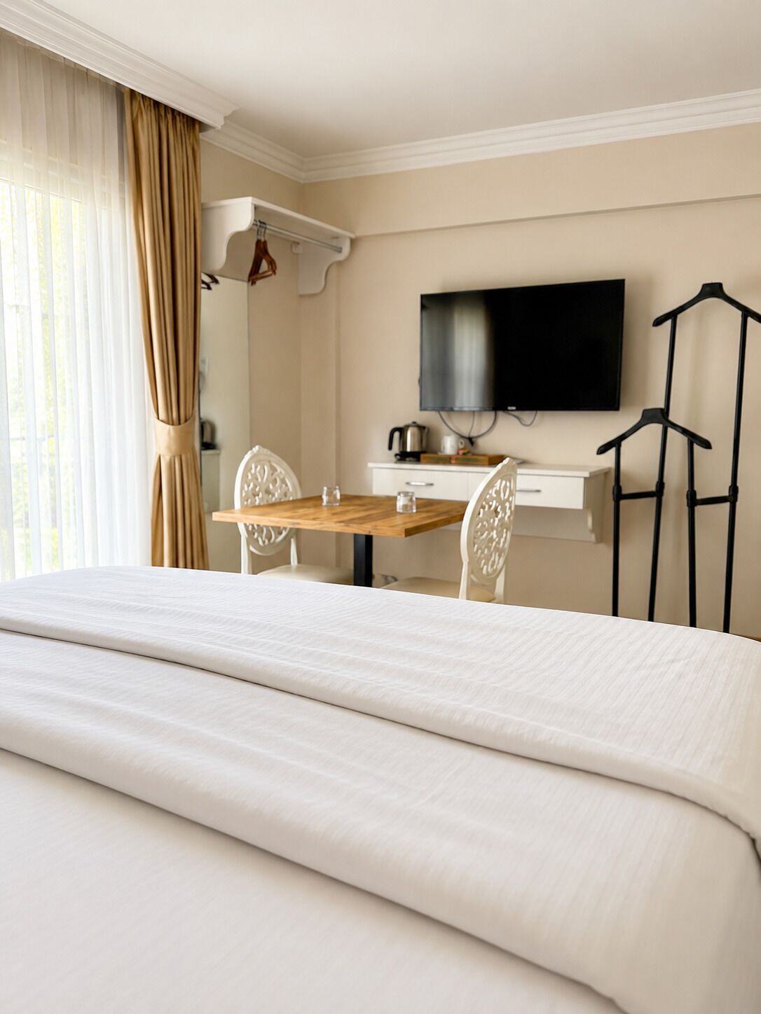Hotellihuone, jossa on sänky, työpöytä tuolilla, televisio ja naulakko.