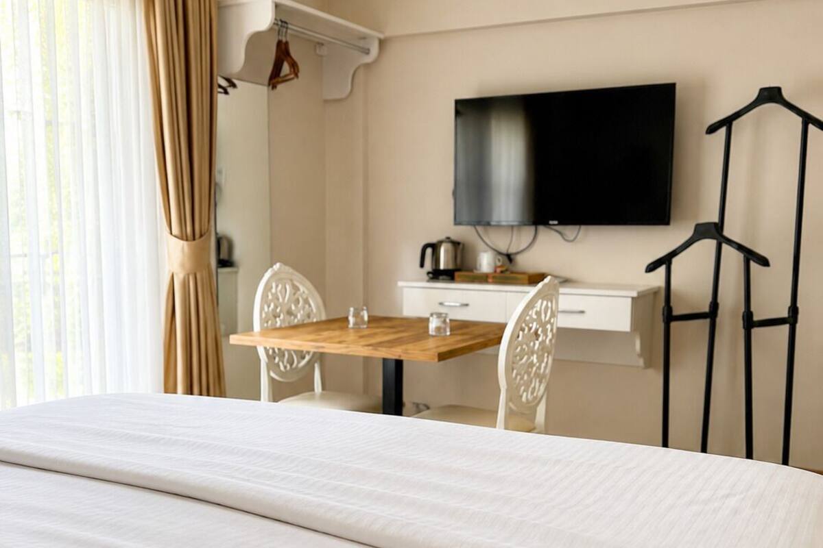 Una habitación de hotel con una cama, un escritorio con silla, televisión y perchero.
