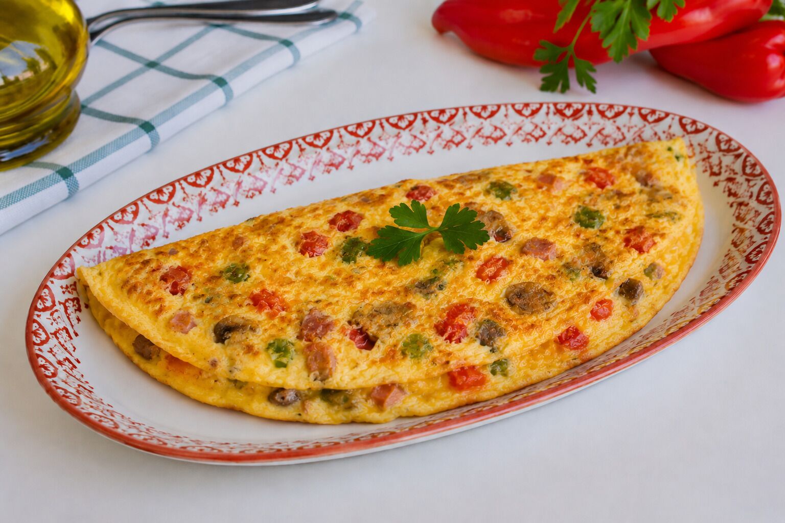 A plate with a food item, a patterned tablecloth, and red peppers in the background.