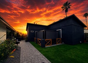 Een modern huis met een overdekte patio, een gazon en een zonsonderganglucht.