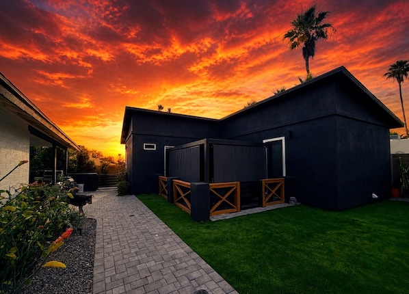Une maison moderne dotée d’un patio couvert, d’une pelouse et offrant une vue sur un ciel au coucher du soleil.