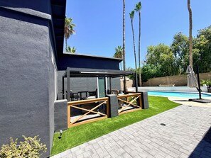Een modern terras buiten met een zwembad, omgeven door palmbomen en een verzorgd gazon.