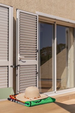 A sliding glass door with a view of a house, a green chair, and a hat on a cushion.
