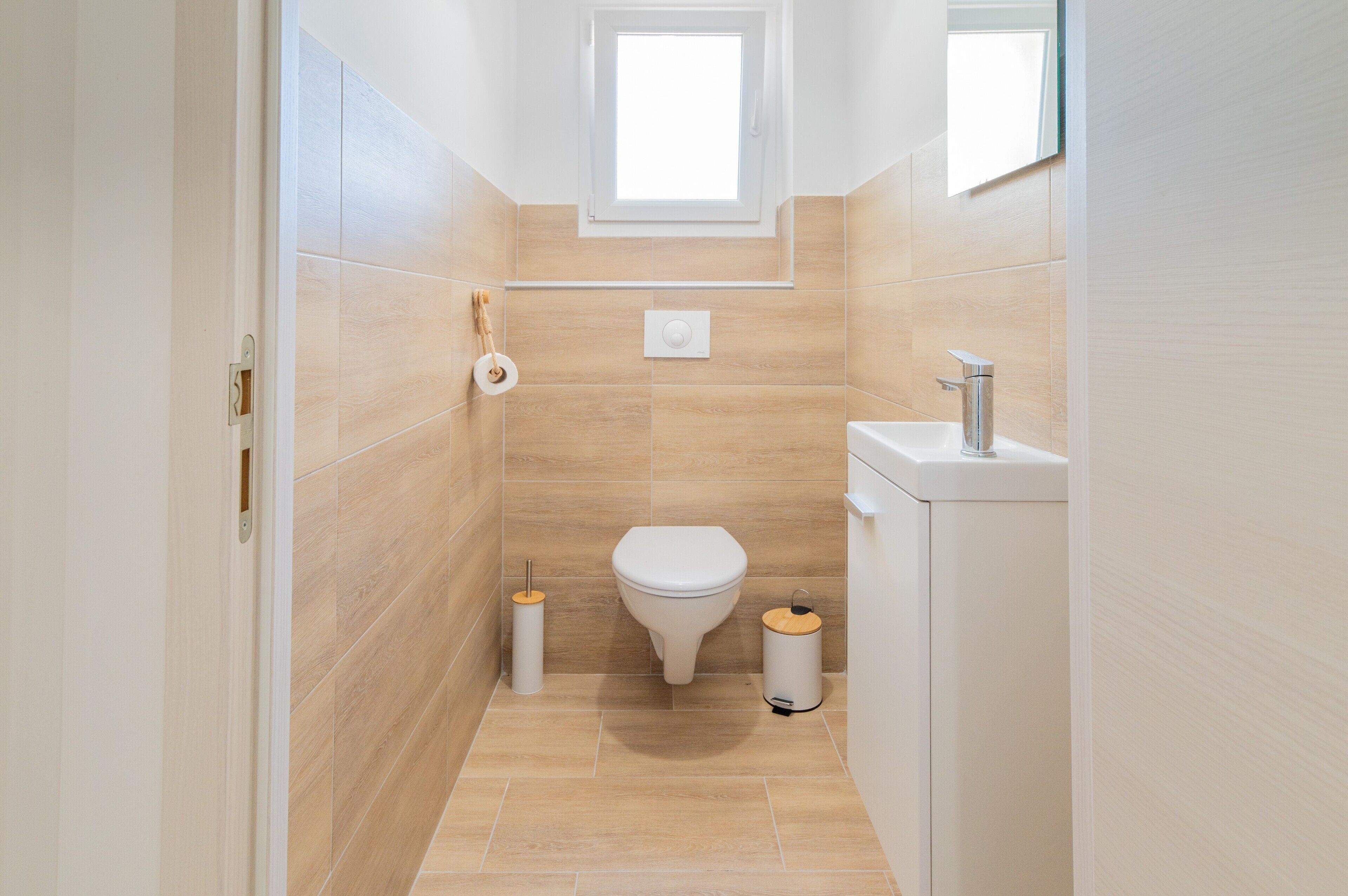 Et badeværelse med toilet, bidet og vask, fliserede vægge og et lille vindue.
