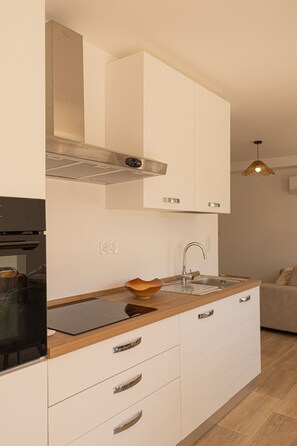 A modern kitchen with white cabinets, a stainless steel range hood, a wooden countertop, and a built-in oven.