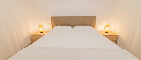 A neatly made bed with a tufted headboard, two bedside lamps, and a plain wall.