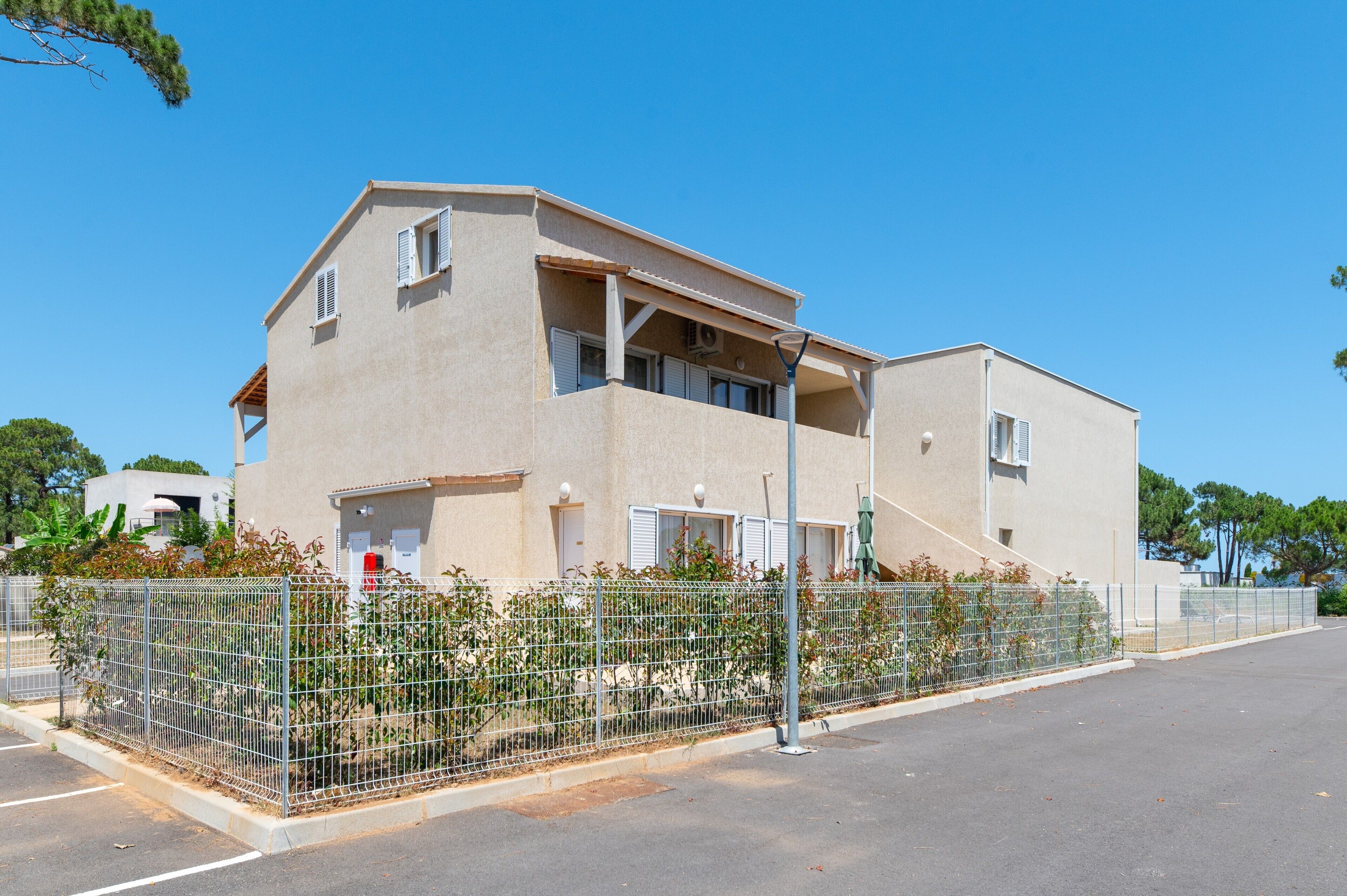 A two-story building with a balcony, a fenced garden area, and a clear sky.