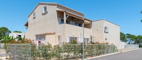 A two-story building with a balcony, a fenced garden area, and a clear sky.