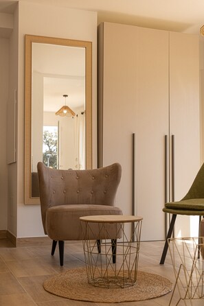 A room with a large mirror, a brown upholstered chair, a round table with a woven base, and a green chair with a round table.