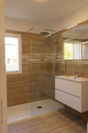 Un baño moderno con ducha envuelta en vidrio, tocador con espejo y ventana que deja entrar luz natural.