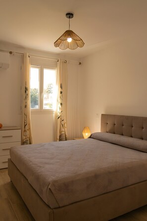 Un dormitorio con una cama, una lámpara de noche, una ventana con cortinas y una lámpara colgante.