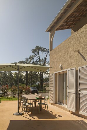 Un patio al aire libre con una mesa y sillas, una sombrilla y un edificio con persianas.