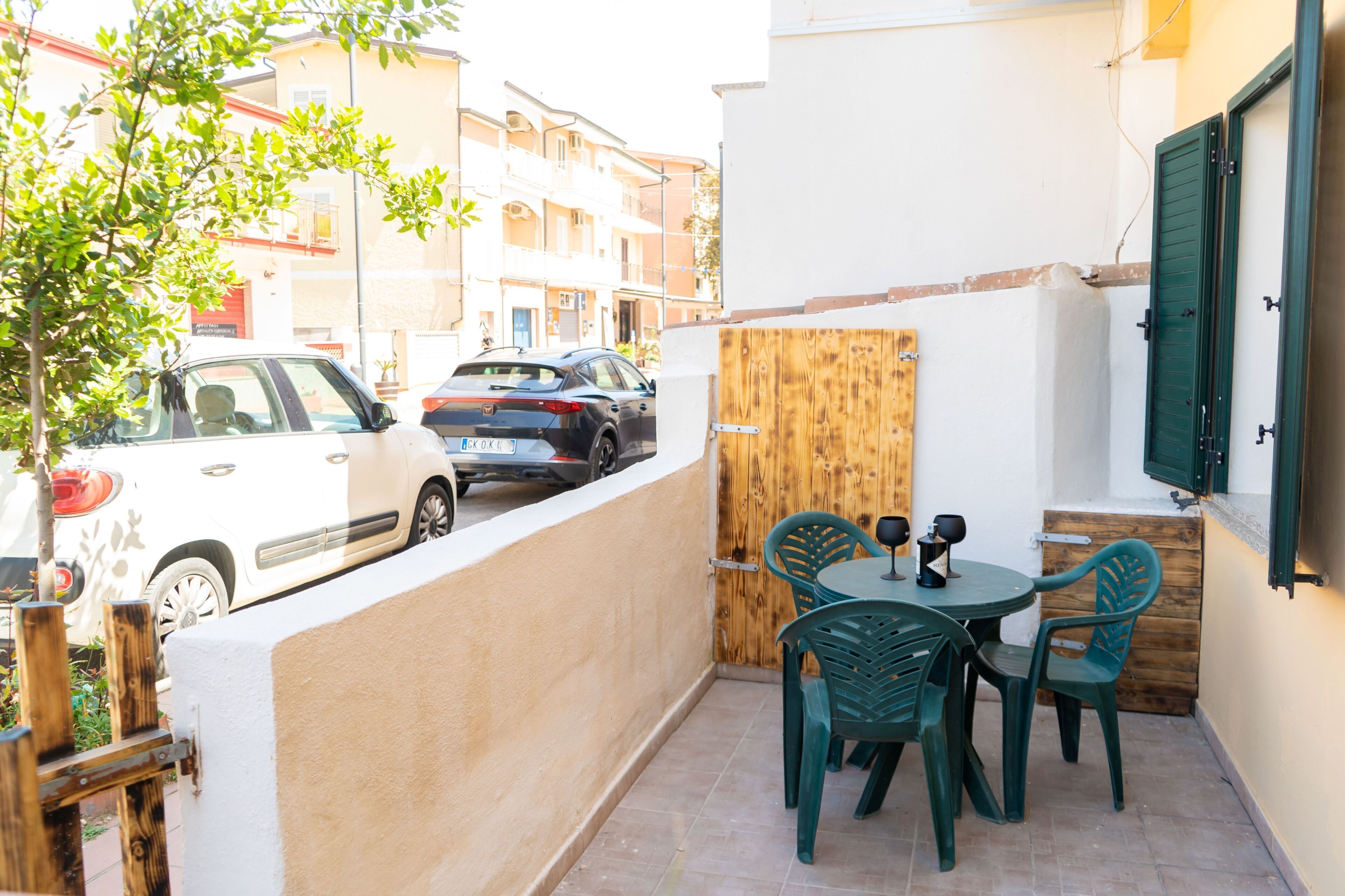 Eine kleine Terrasse im Freien mit Tisch und Stühlen, einem Holzzaun und parkenden Autos im Hintergrund.