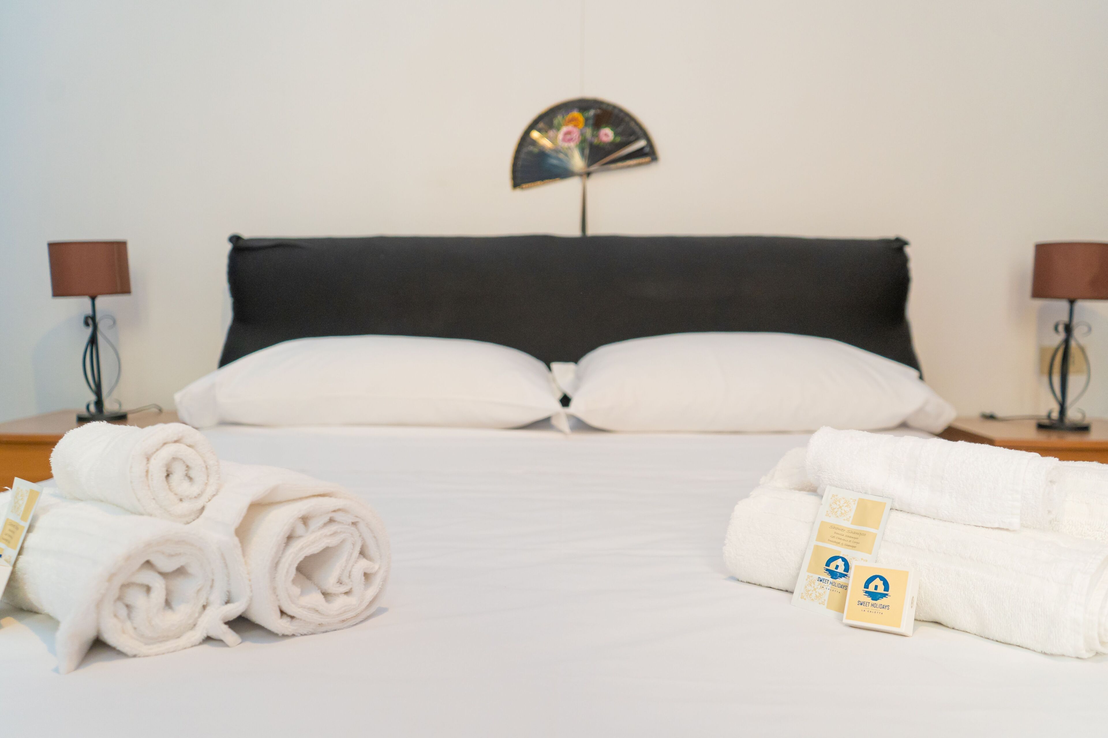 A neatly made bed with white linens, two pillows, and a decorative wall fan.