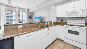 A modern kitchen with white cabinetry, a granite countertop, a built-in dishwasher, a microwave, and an oven. - 🌊Beachfront Complex~Large Lagoon Pool~Shores of Panama 1509🌊 (Panama City Beach)