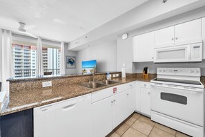 Eine moderne Küche mit weißen Schränken, einer Granit Arbeitsplatte, einem integrierten Geschirrspüler, einer Mikrowelle und einem Backofen.