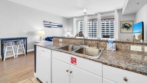 A modern kitchen with a granite countertop, stainless steel sink, and white cabinetry. - 🌊Beachfront Complex~Large Lagoon Pool~Shores of Panama 1509🌊 (Panama City Beach)