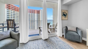 A balcony with a view of high-rise buildings, a seating area with chairs, and a rug on the floor. - 🌊Beachfront Complex~Large Lagoon Pool~Shores of Panama 1509🌊 (Panama City Beach)