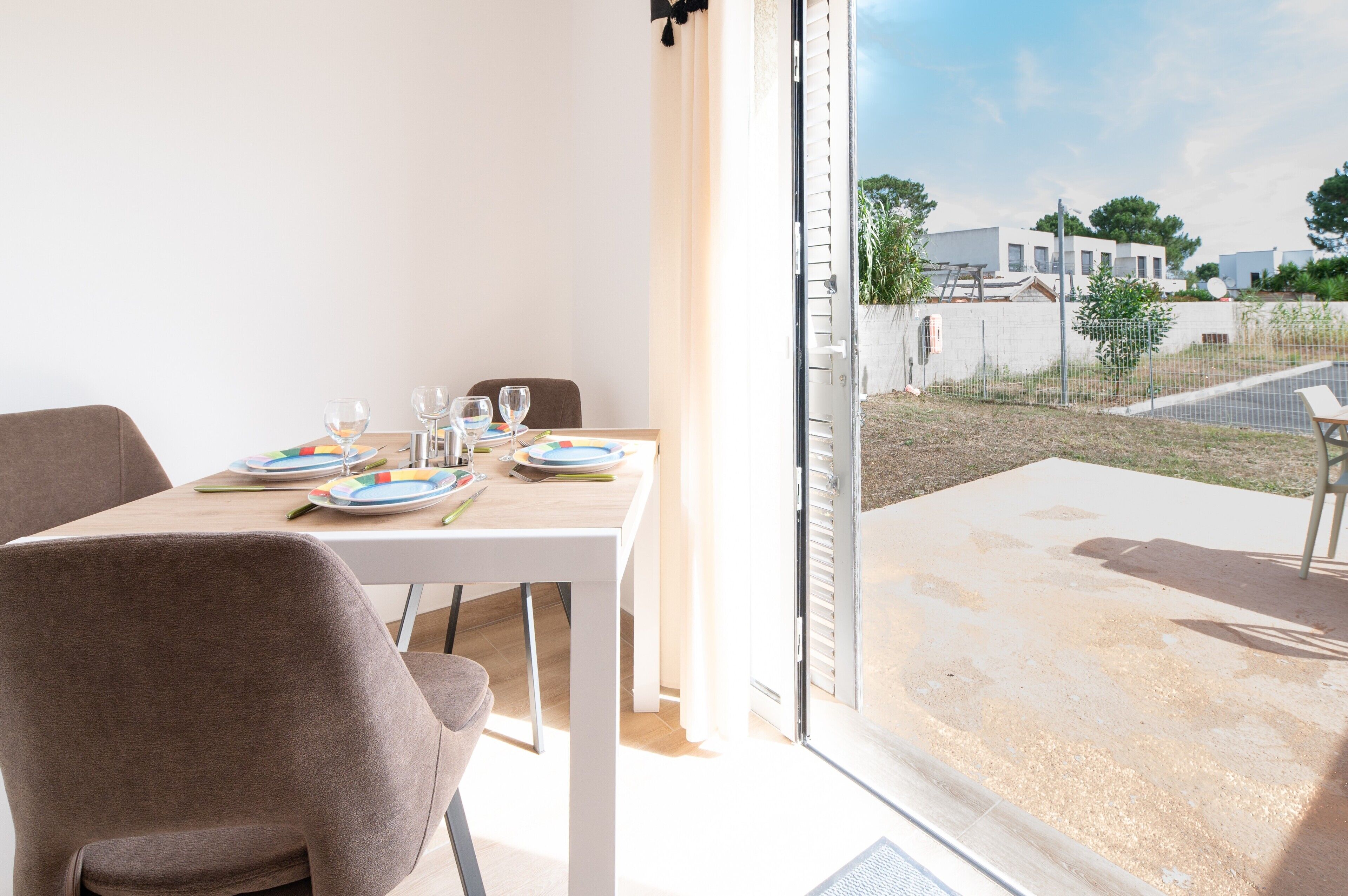 A dining area with a table set for two, a sliding glass door leading to an outdoor patio, and a view of a residential area.