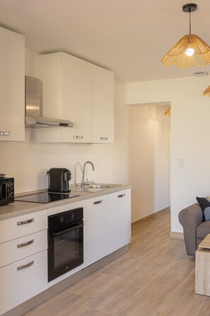 A modern kitchen with white cabinets, a built-in oven, a coffee maker, and a hanging pendant light.