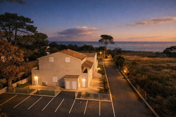 A two-story building with a parking area and a view of the sea at dusk.