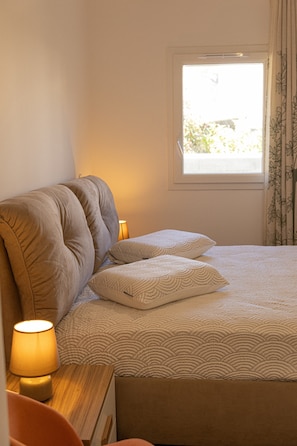 A bedroom with a bed, pillows, a nightstand with a lamp, and a window with curtains. - Apartment 'La Dolce Vita 3' with Sea View, Wi-Fi and Air Conditioning (Borgo)