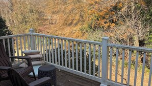 Une terrasse en bois avec une balustrade blanche, des meubles d’extérieur et une vue sur le feuillage automnal.