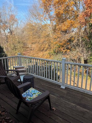Eine Holzterrasse mit weißer Reling, Gartenmöbeln und Blick auf herbstliche Laubfärbung.