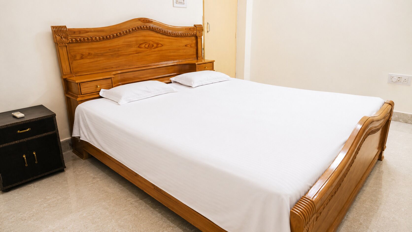 A single bed with a wooden headboard, a bedside table with drawers, and a nightstand with a small cabinet.