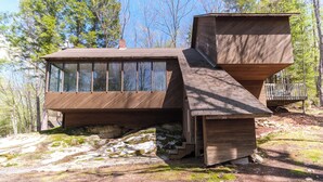 Une cabane moderne en bois, dotée de grandes fenêtres, d’un toit à pente et d’une terrasse en bois.