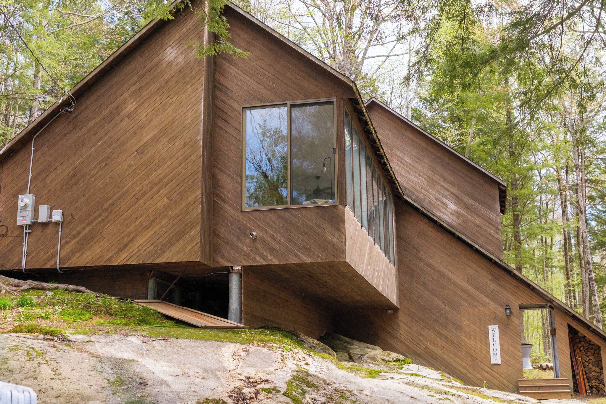 A modern wooden cabin with a sloped roof, large windows, and a stone foundation.
