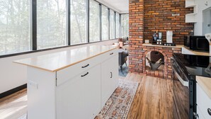 Une cuisine moderne avec un mur en briques, de grandes fenêtres et un plan de travail en bois.
