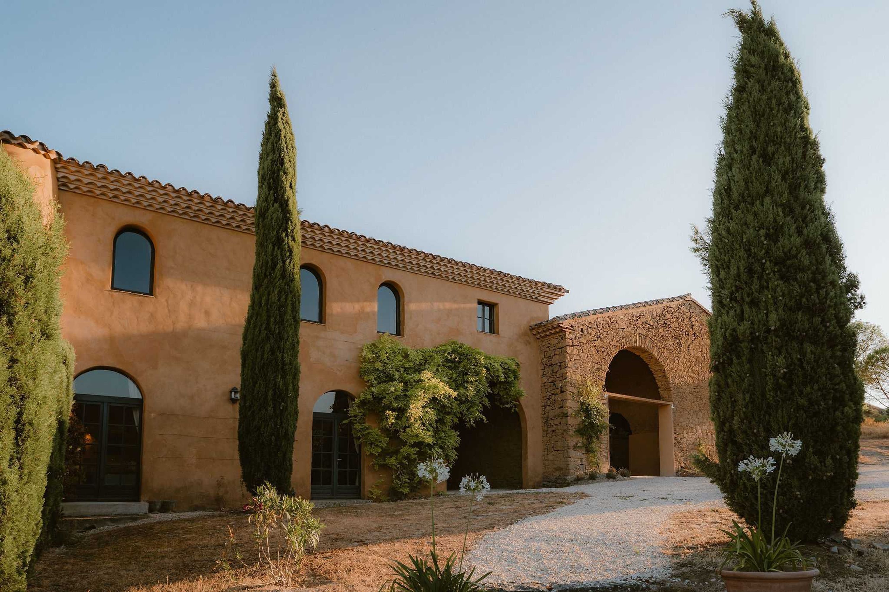 A building with a tiled roof, multiple arched doorways, and tall cypress trees.