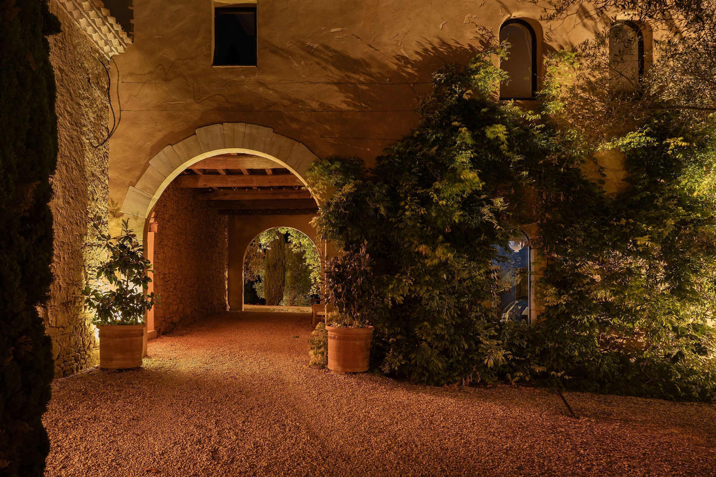 An arched corridor with a gravel path, surrounded by greenery and stone walls.