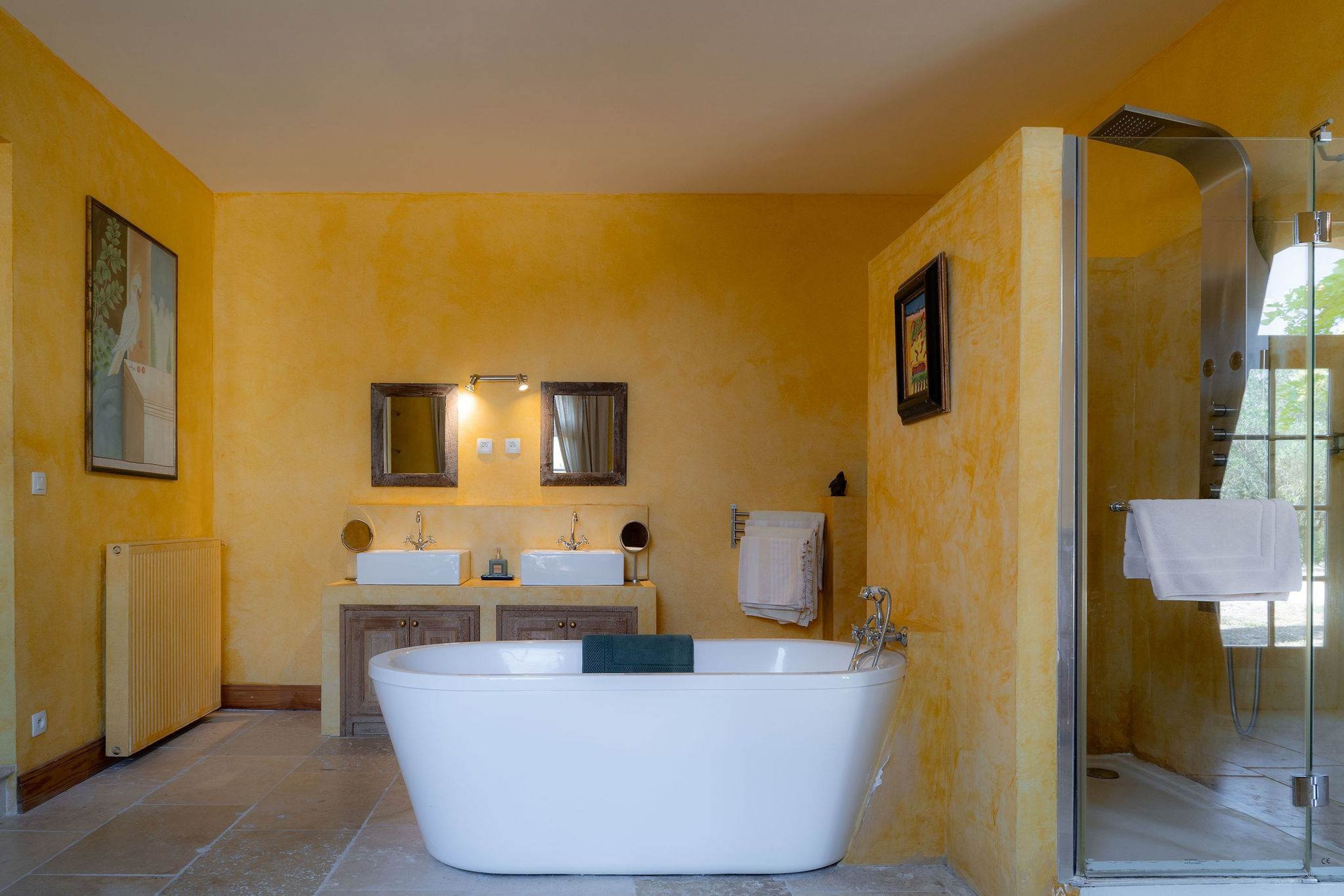 A bathroom with a freestanding bathtub, two sinks, a glass shower enclosure, and a radiator.