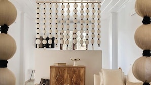 A modern living room with a round wooden table, a sofa, a cabinet, and a decorative wall panel. - Angelina Aegina Escape (Aegina)