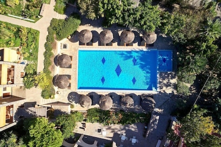 An aerial view of a resort with a central swimming pool, surrounded by lounge chairs and umbrellas, and lush greenery.. Angelina Aegina Escape