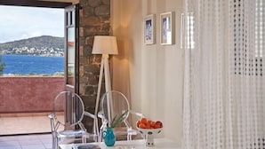 A room with a view of the sea, a stone wall, a table with a lamp, chairs, and framed pictures. - Angelina Aegina Escape (Aegina)
