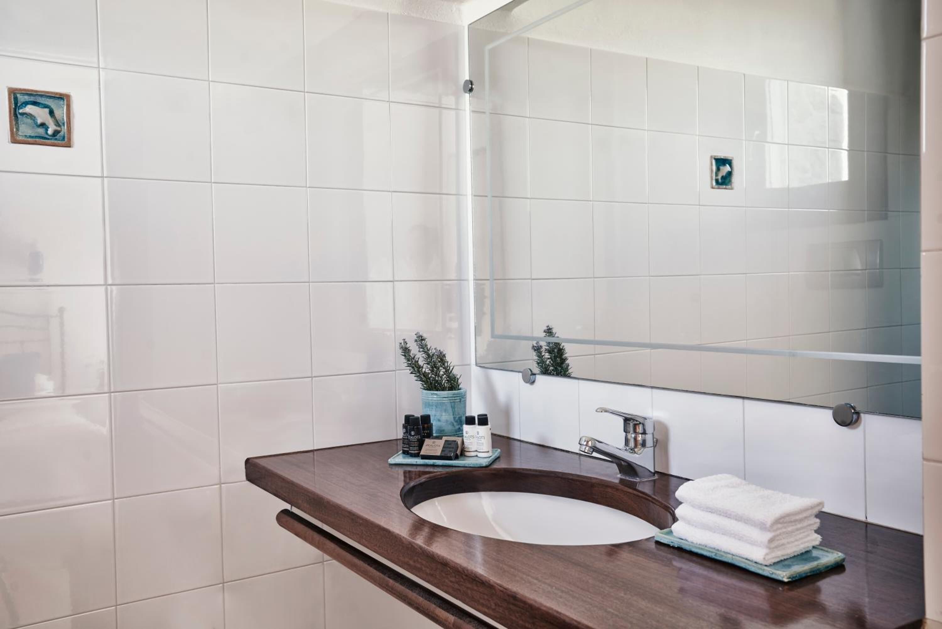 Un baño con baldosas blancas, encimera de madera, lavamanos, espejo y una planta pequeña.