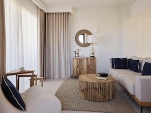 Habitación de hotel con sofá, una mesita redonda, un aparador de madera, un espejo circular y una lámpara.