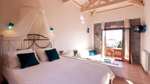A bedroom with a canopy bed, a stone wall, a TV, and a view to the outside. - Angelina Aegina Escape (Aegina)