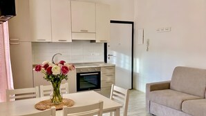 Una cocina moderna con armarios blancos, una mesa de comedor con sillas, un jarrón de flores y un sofá beige en la sala.