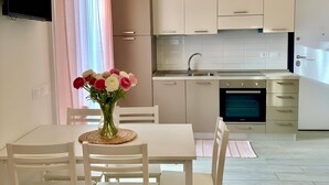 Una cocina moderna con armarios blancos, horno empotrado y comedor con mesa y sillas.