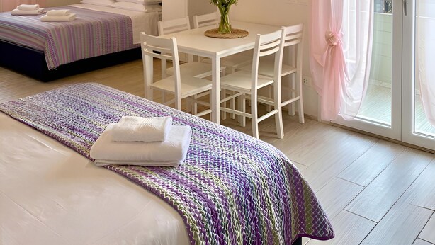 Habitación de hotel con dos camas, una mesa de comedor con sillas, un televisor montado en la pared y un ventanal corredero que da a un espacio exterior.
