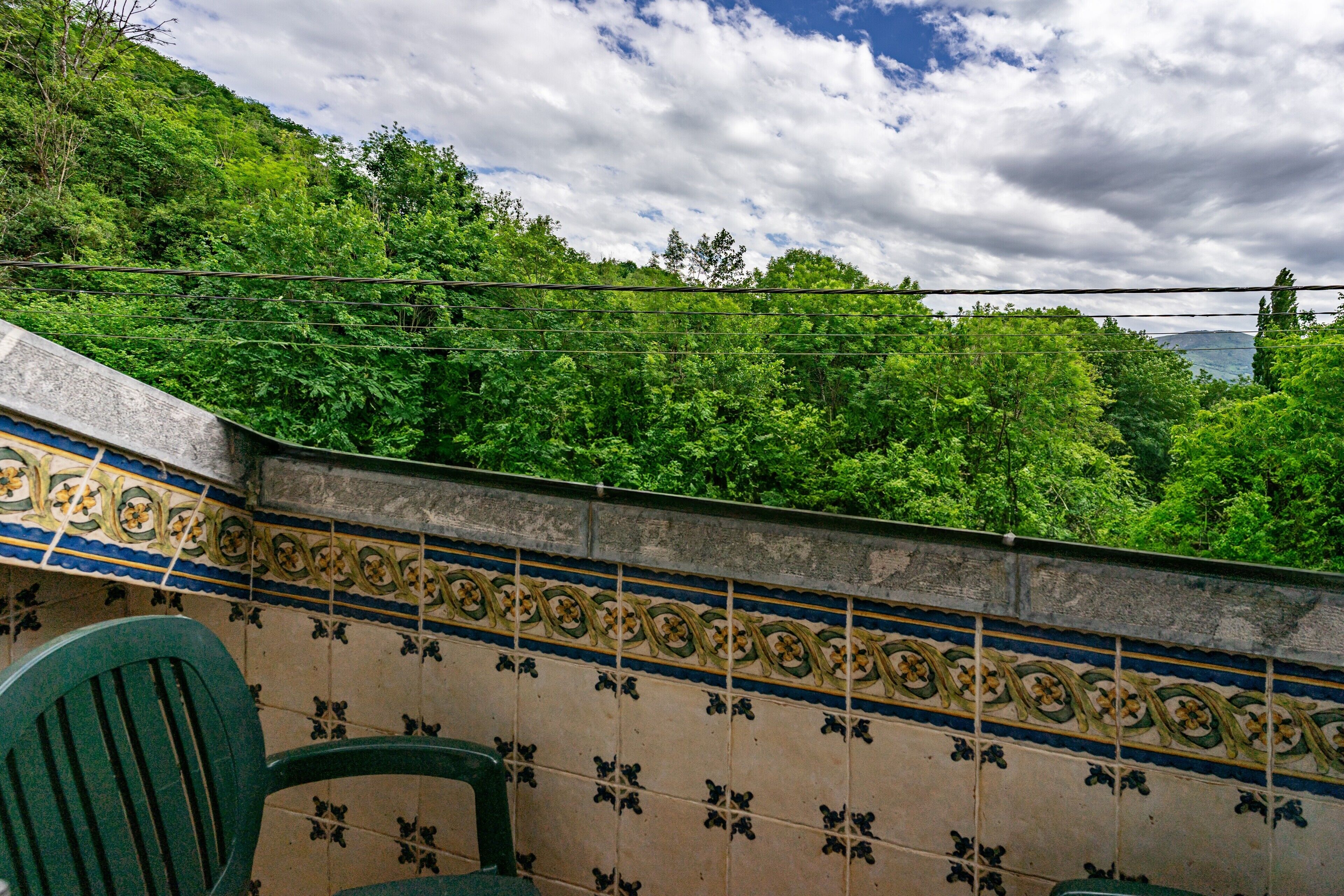A tiled wall with a decorative pattern, a green chair, and a view of a lush green hillside.