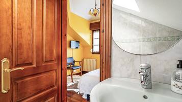 A wooden door, a white sink, a mirror, a bed, a chair, and a television in a room.