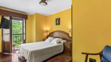 Un dormitorio con cama, mesitas de noche de madera, televisor, ventana con cortinas y puerta.